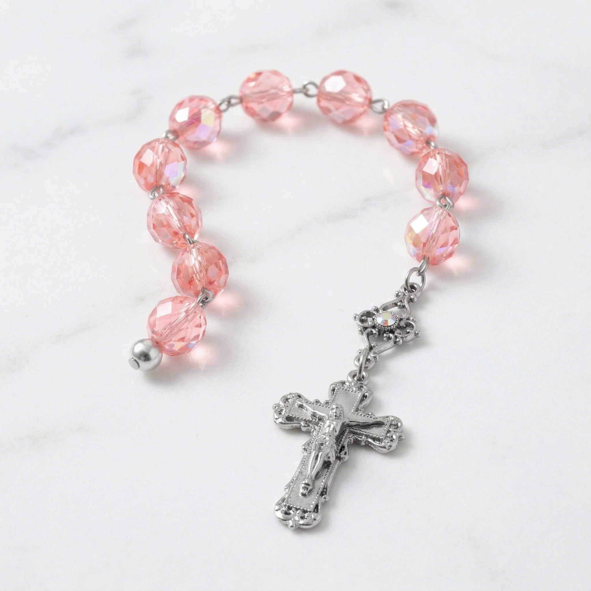 Pink rosary bracelet with a silver cross on a marble surface