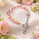Pink rosary with silver cross on a soft fabric background with flowers