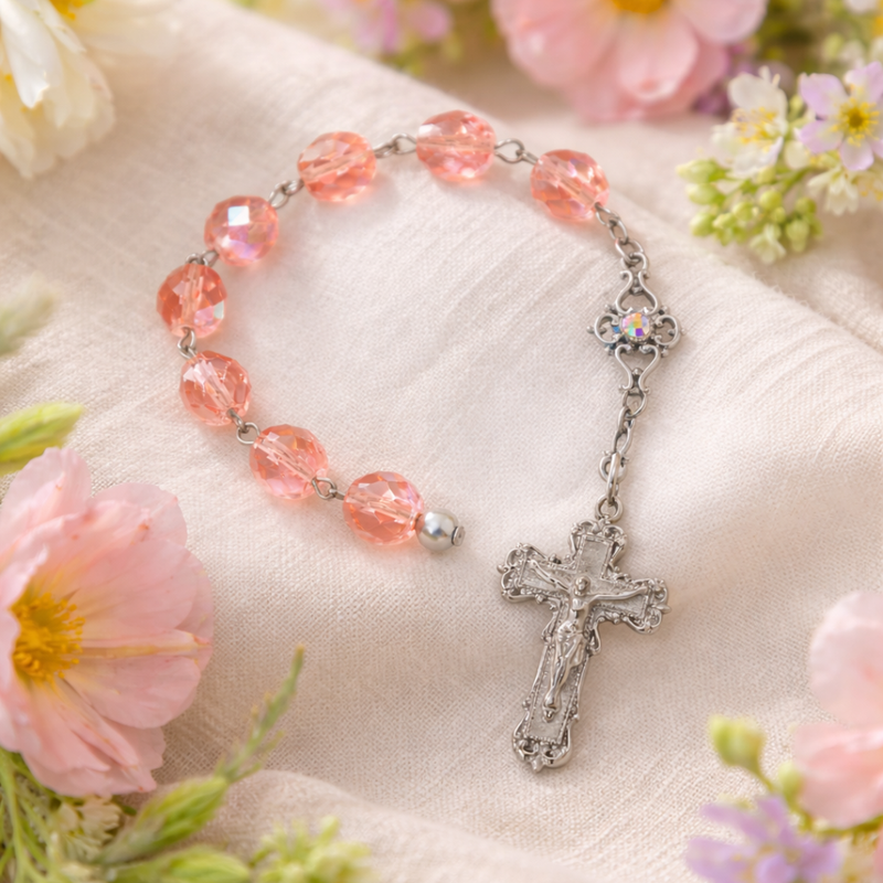 Pink rosary with silver cross on a soft fabric background with flowers