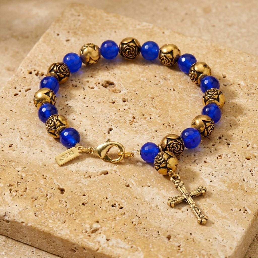 Sapphire & Gold Rosebud Beaded Cross Charm Bracelet displayed on a textured beige stone tile.