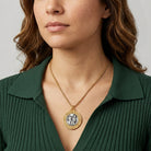 Woman wearing a gold tone necklace with a St. Christopher medallion pendant against a neutral background