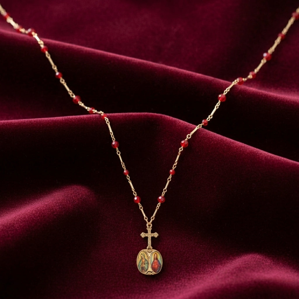 Gold necklace with red beads and a cross pendant featuring religious motifs on a burgundy fabric background