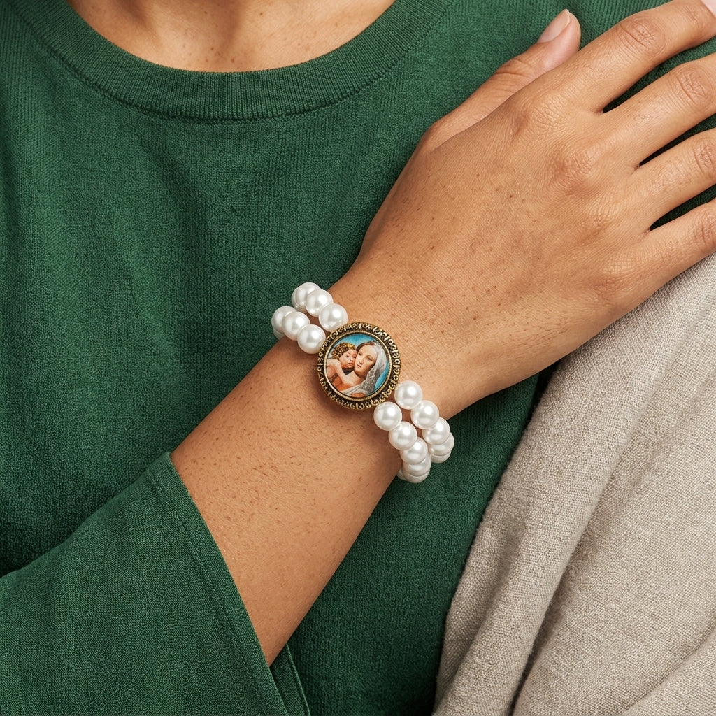 Pearl bracelet with a circular Mary and Child emblem worn on a wrist against a green shirt.