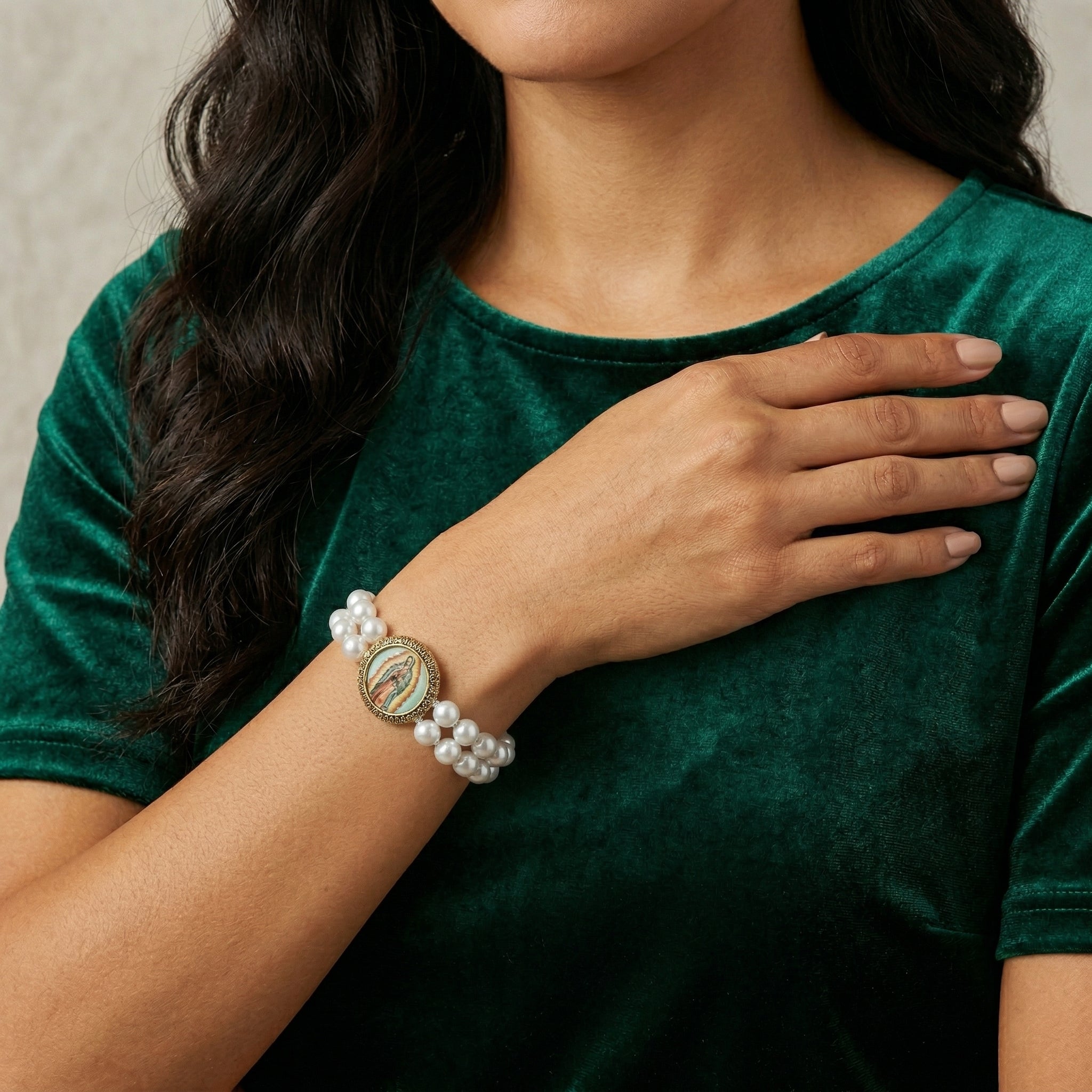 Woman wearing a green shirt and faux pearl bracelet with a circular Lady of Guadalupe emblem.