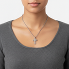 Person wearing a silver cross necklace on a plain background
