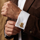 Close-up of a person wearing a brown jacket with a gold cowboy boot cufflink on a white shirt.