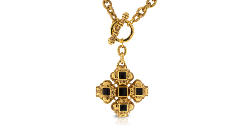 A gold-tone cross pendant necklace with four black square stones in the center of each arm, hanging from a gold chain on a plain white background.